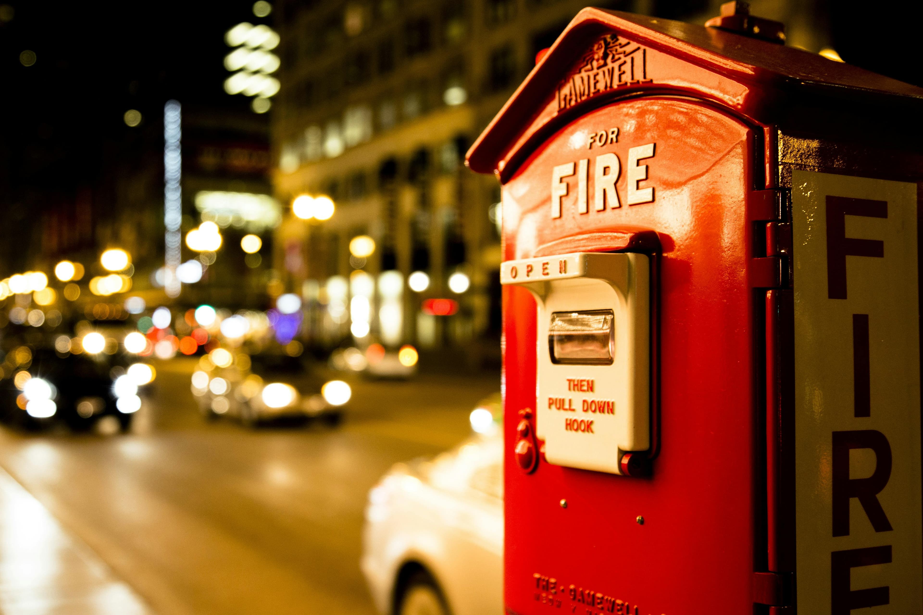 A fire alarm pull station sitting on the side of a busy city street with the word FIRE in large bold letters.